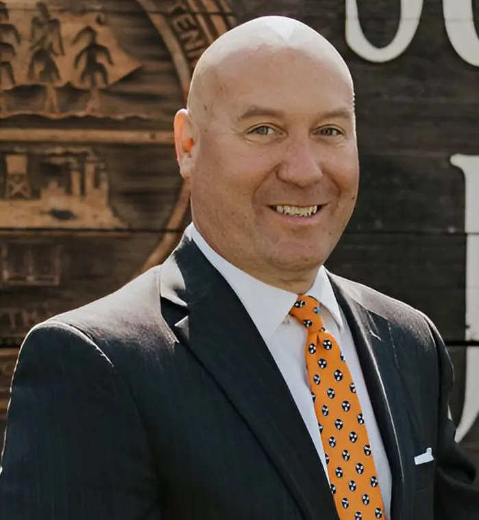 Smiling man in suit with orange tie.