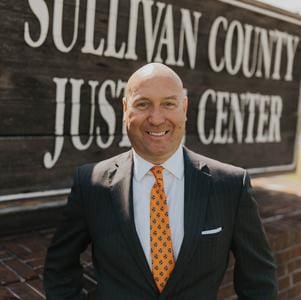 Man in suit smiling in front of courthouse.