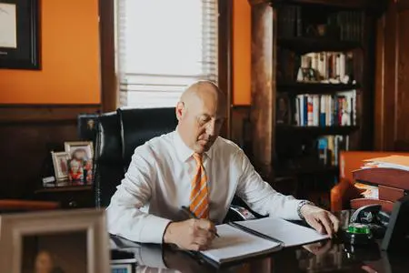 Man in white shirt signing documents at desk.